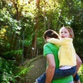 A girl in a yellow shirt getting a piggyback by a woman in a green shirt through a rainforrest path