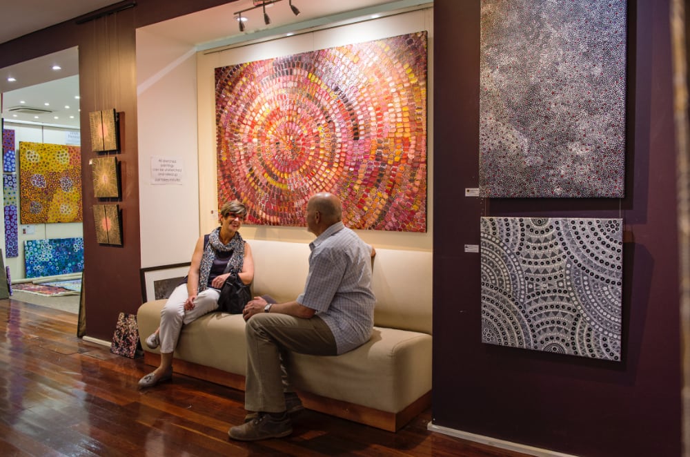Couple on a seat in front of Aboriginal artworks hanging on gallery wall